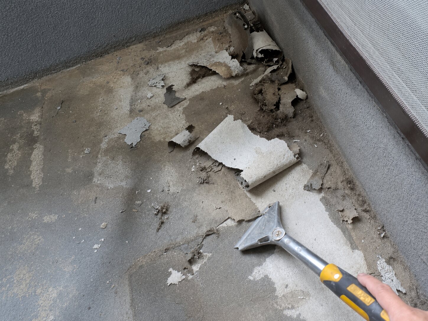 既存塗膜が大きく剥がれ、スクレーパーで撤去しているベランダ床