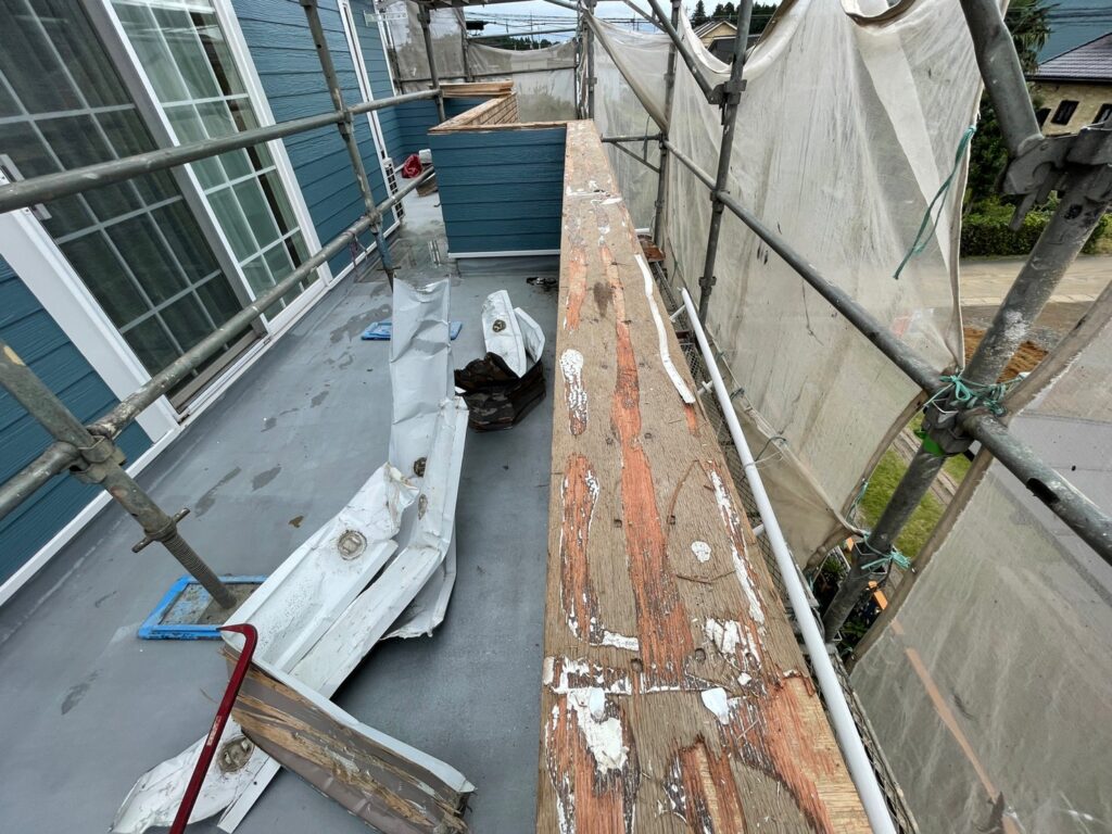 ベランダ手すり壁の笠木を撤去し、上部の木下地が露出した施工状況。撤去した板金部材が床に置かれている